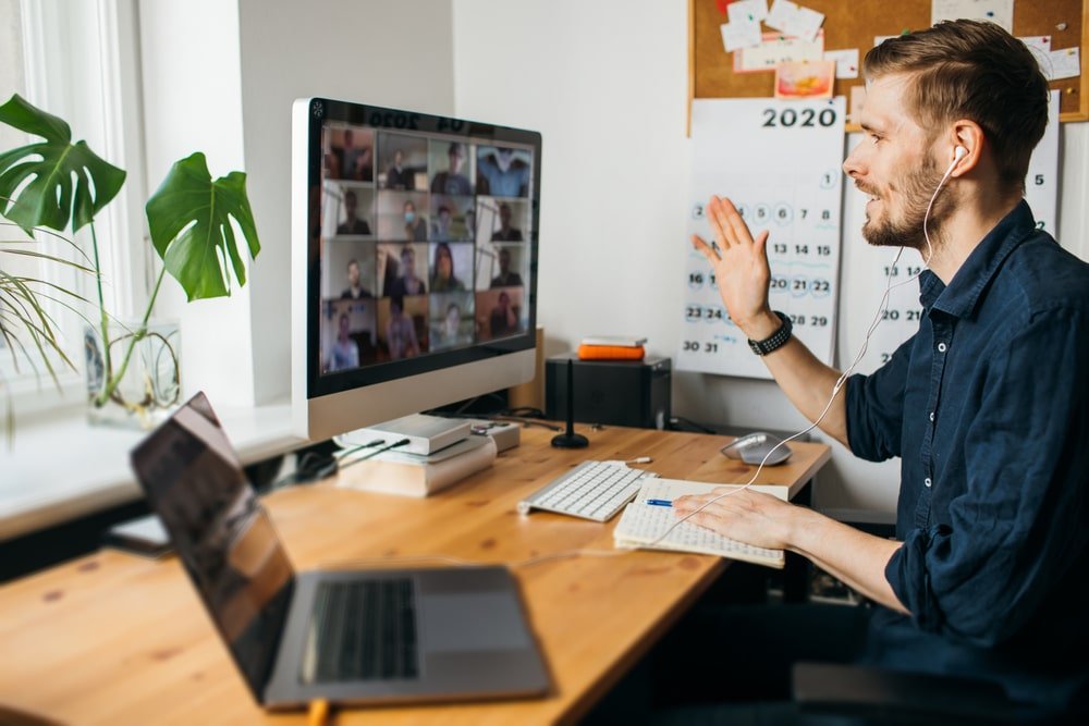 Man zwaait tijdens grote online vergadering op zijn computer.
