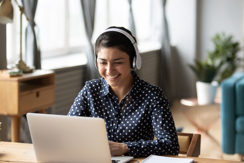 Vrouw glimlacht tijdens online vergadering met laptop en koptelefoon.