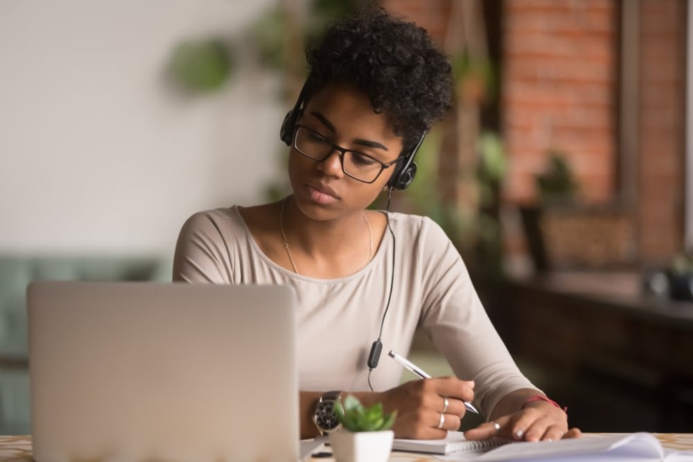 Zakelijke vrouw met headset maakt notities tijdens online werk.
